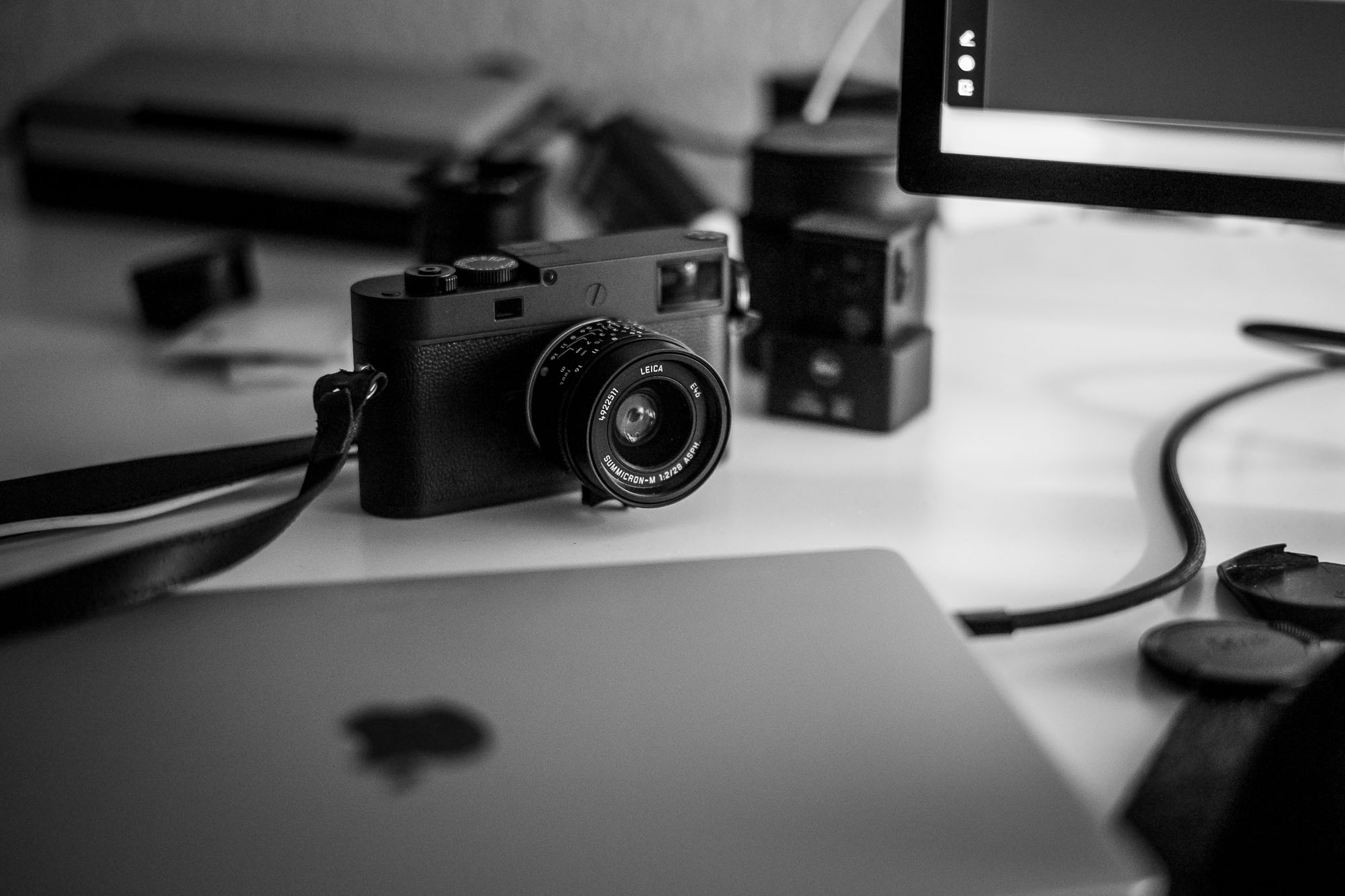 A camera on a desk, with a laptop in front of it and part of a monitor to the side